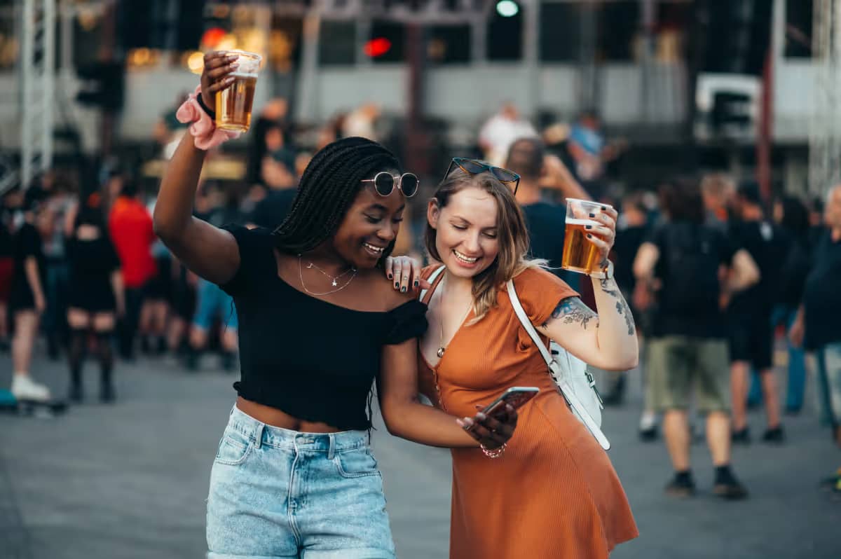 Two women are having a good time at an event and order food and drinks via a smartphone.